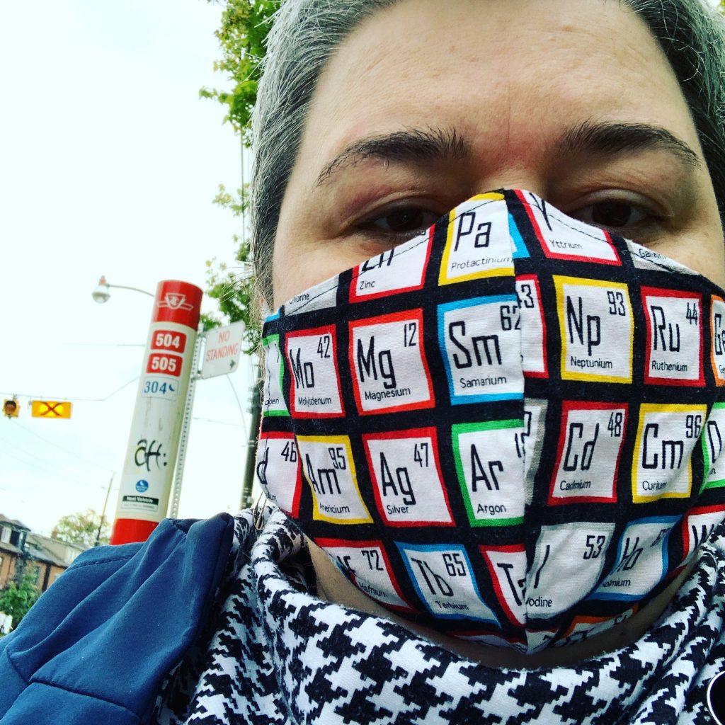 Grey haired female with a periodic table of elements mask and a TTC stop in the background